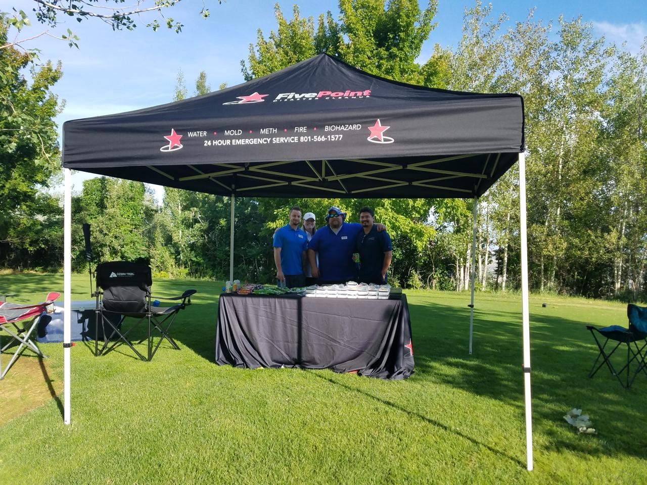 Four Five Point Restoration team members at a branded canopy tent during a community outreach event